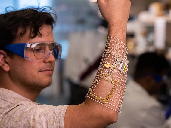 student, wearing safety glasses, holding up arm with biomedical device