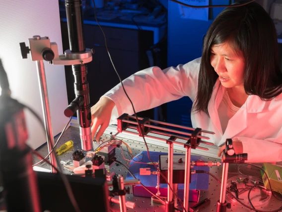 A woman in a lab coat leans over technology.