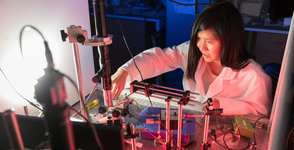 A woman in a lab coat leans over technology.