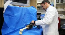 A man in a white lab coat manipulates a device placed on a blue surgical sheet.