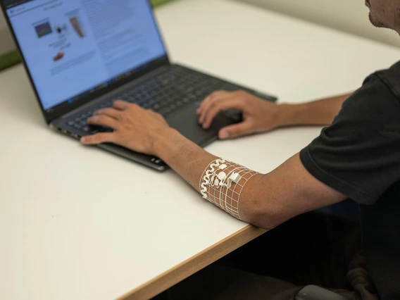 A man types on a computer while wearing a transparent arm cuff.