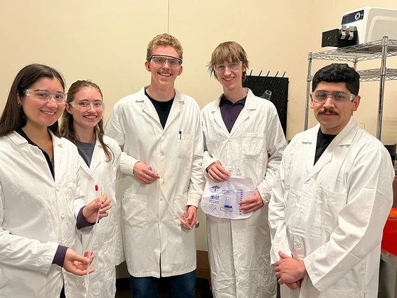 Five students pose for a photo in lab coats.