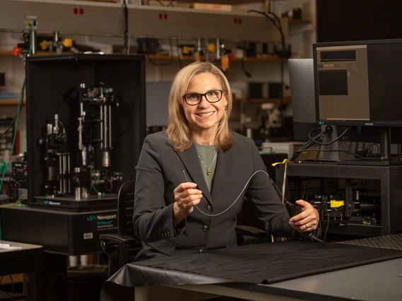 A woman with blond hair holds up a really tiny microscope.