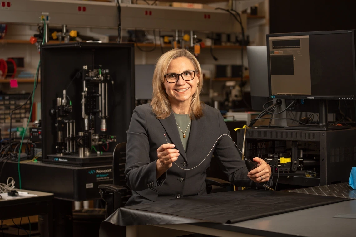 A woman with blond hair holds up a really tiny microscope.