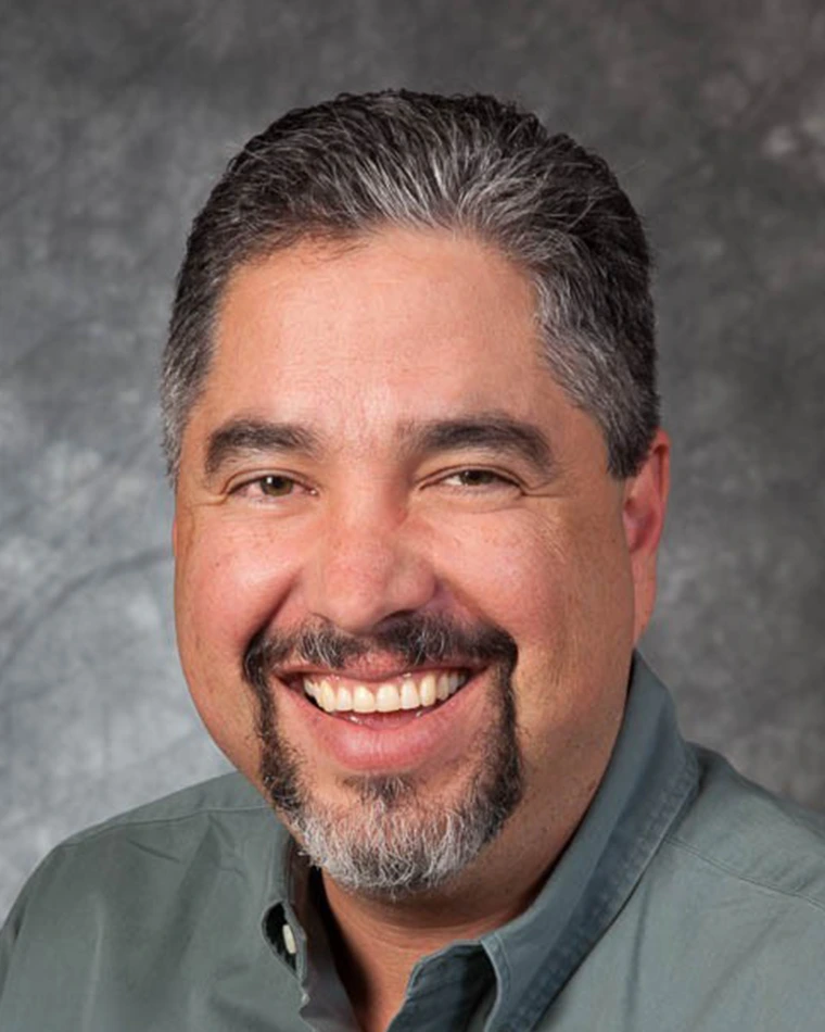 person with short, dark graying hair and beard wearing green shirt