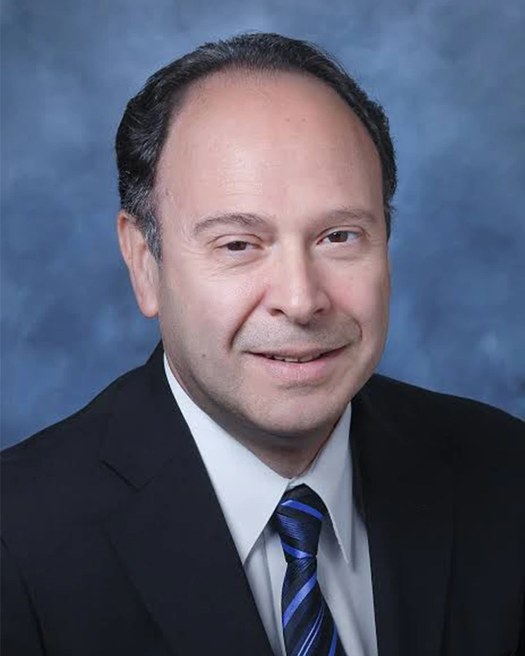 person with short dark hair, wearing dark business suit, white shirt and striped blue tie