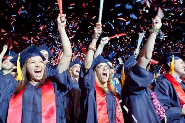 group of cheering students in graduation regalia