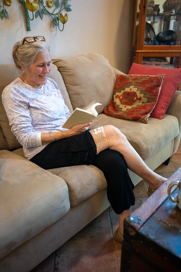 An older women sits in a couch with a small cuff device on her leg.