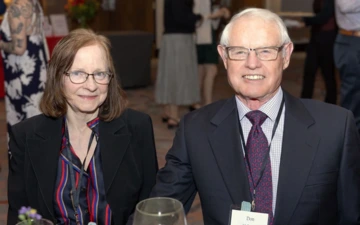 two smiling people, wearing glasses, seated at a table